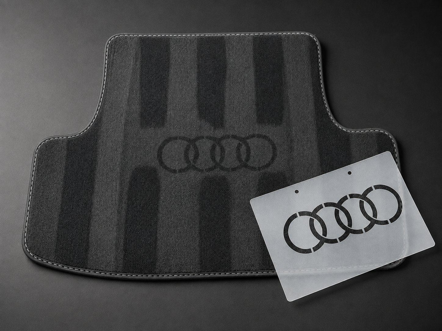 Audi stencil positioned beside its finished logo effect on a black car mat